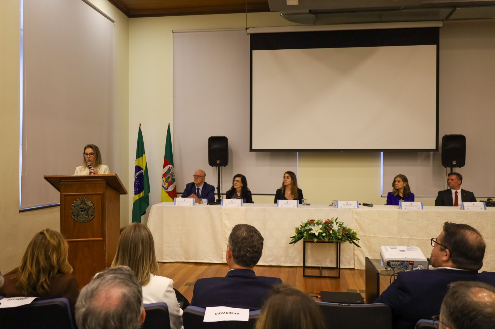 A foto mostra a imagem da nova procuradora discursando.