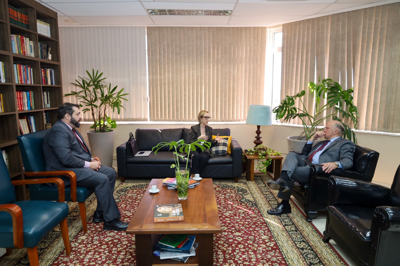 A foto mostra os desembargadores Martins Costa e Alexandre sentados em poltronas conversando com a professora helena, também sentada.
