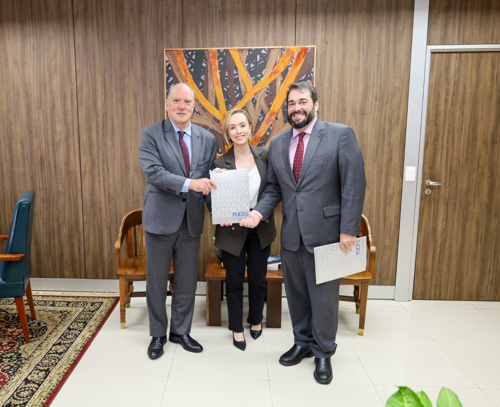 A foto mostra os desembargadores Martins Costa e Alexandre posando para foto com a professora helena.