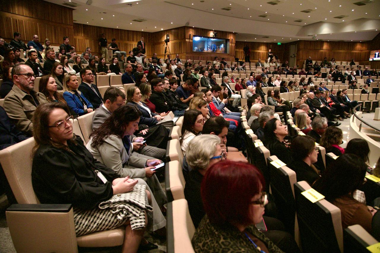 Público acompanha a mesa de abertura da Semana da Conciliação Trabalhista no plenário Milton Varela Dutra, no Tribunal Regional do Trabalho da 4ª Região (TRT-RS). A plateia está composta por magistrados, servidores, advogados, estudantes e demais convidados, com o auditório praticamente lotado. A imagem mostra a diversidade de participantes, atentos ao evento, em um ambiente formal e bem iluminado.