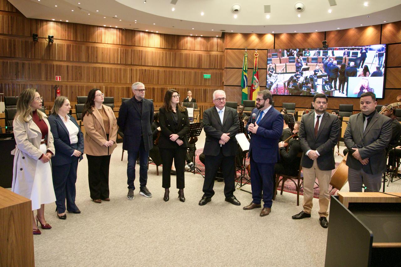 erimônia de encerramento da mediação coletiva no plenário do TRT-RS, com nove pessoas em pé, lado a lado, formalizando o acordo que pôs fim à greve no transporte público de Esteio. O vice-presidente do TRT-RS, Alexandre Cruz, segura o microfone e discursa. 