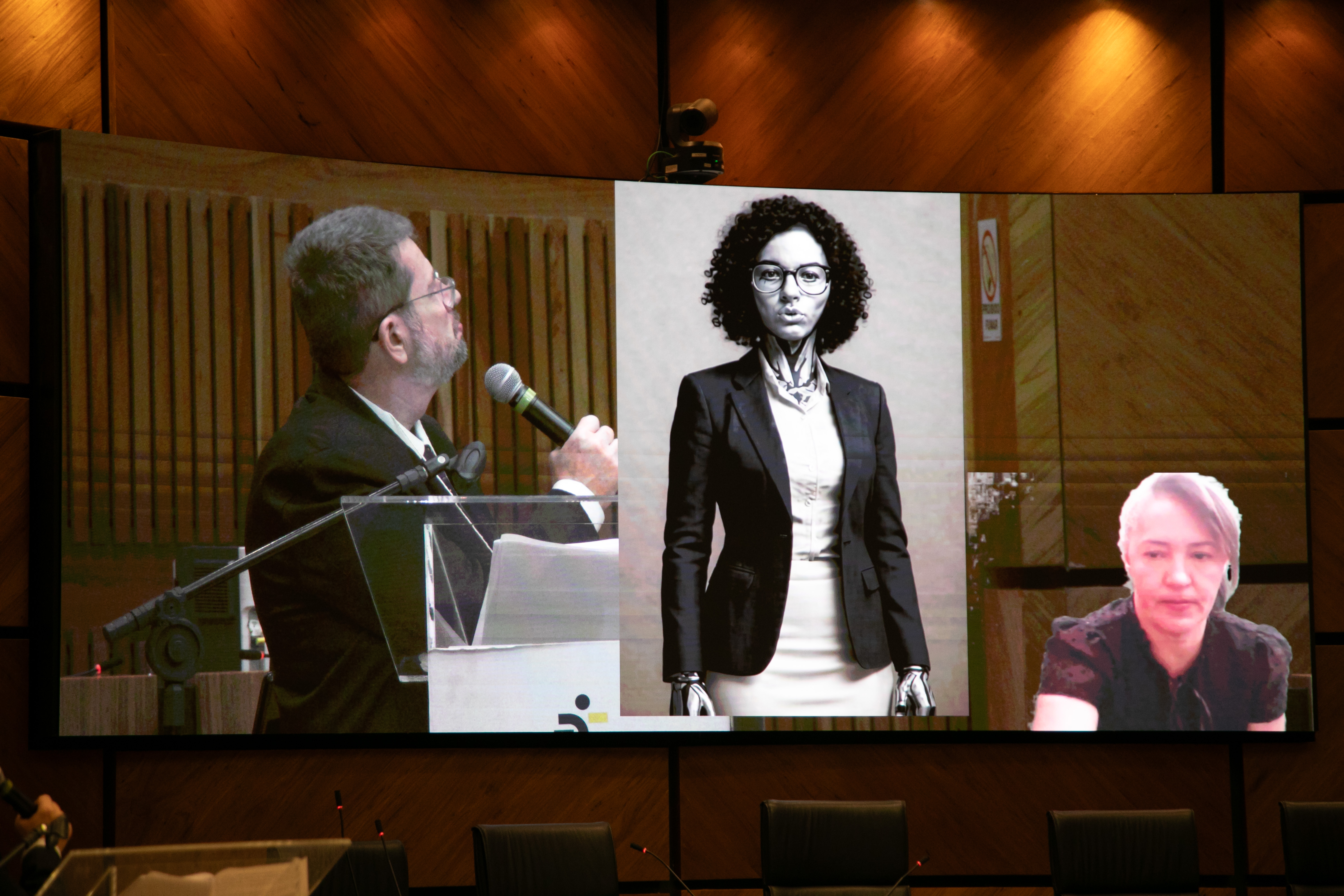 Juiz Selbach, em primeiro plano, conversando com a S.A.R.A, pelo telão