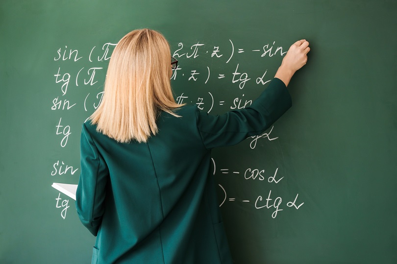 Foto ilustrativa de uma professora que está escrevendo em um quadro de giz