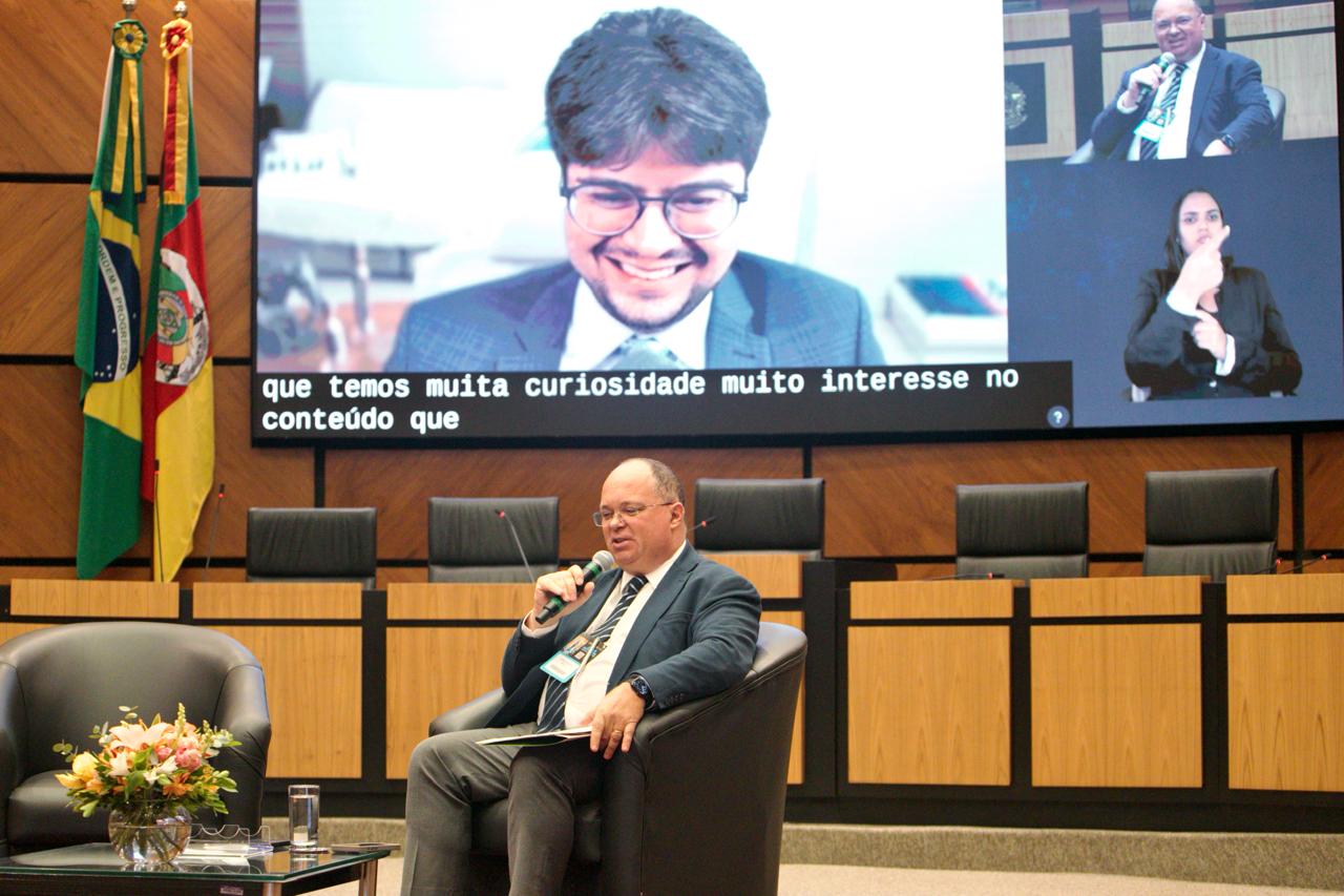 João Valério aparece no telão, ao fundo. Na frente dele, o juiz Jorge Alberto está sentado em um sofá e fala ao microfone.