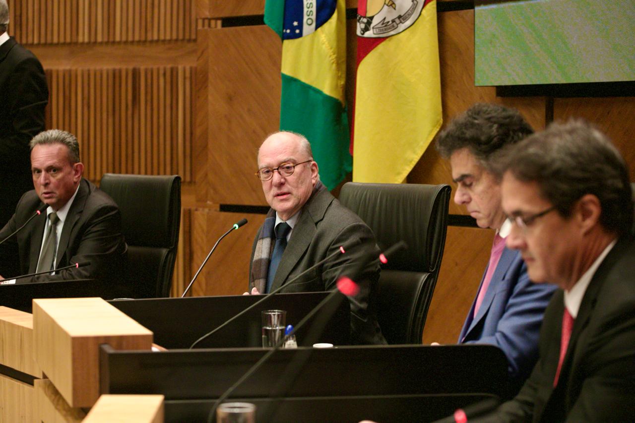 O corregedor-geral da Justiça do Trabalho, ministro Luiz Philippe Vieira de Mello Filho, fala durante evento no Plenário Milton Varela Dutra. Ao seu lado, estão o presidente do TRT-RS, desembargador Ricardo Martins Costa, o assessor Cláudio Gomes Carneiro e outro participante. Ao fundo, aparecem as bandeiras do Brasil e do Rio Grande do Sul.