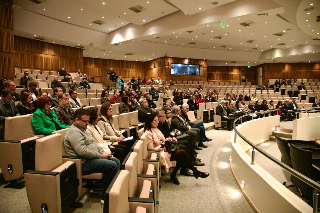 Público presente no encerramento da correição, no Plenário Milton Varela Plenário do TRT-RS durante uma correição. Várias pessoas estão sentadas assistindo à atividade, em um auditório grande com cadeiras claras e paredes de madeira. O clima é sério e tranquilo.