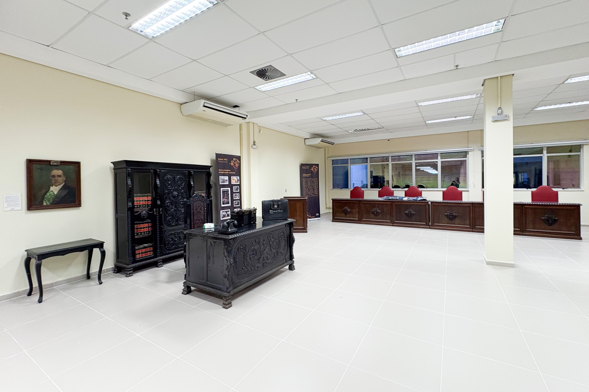 Quadro de Getúlio Vargas na parede à esquerda, diversos mobiliários antigos e uma bancada antiga com poltronas vermelhas no fundo à direita.