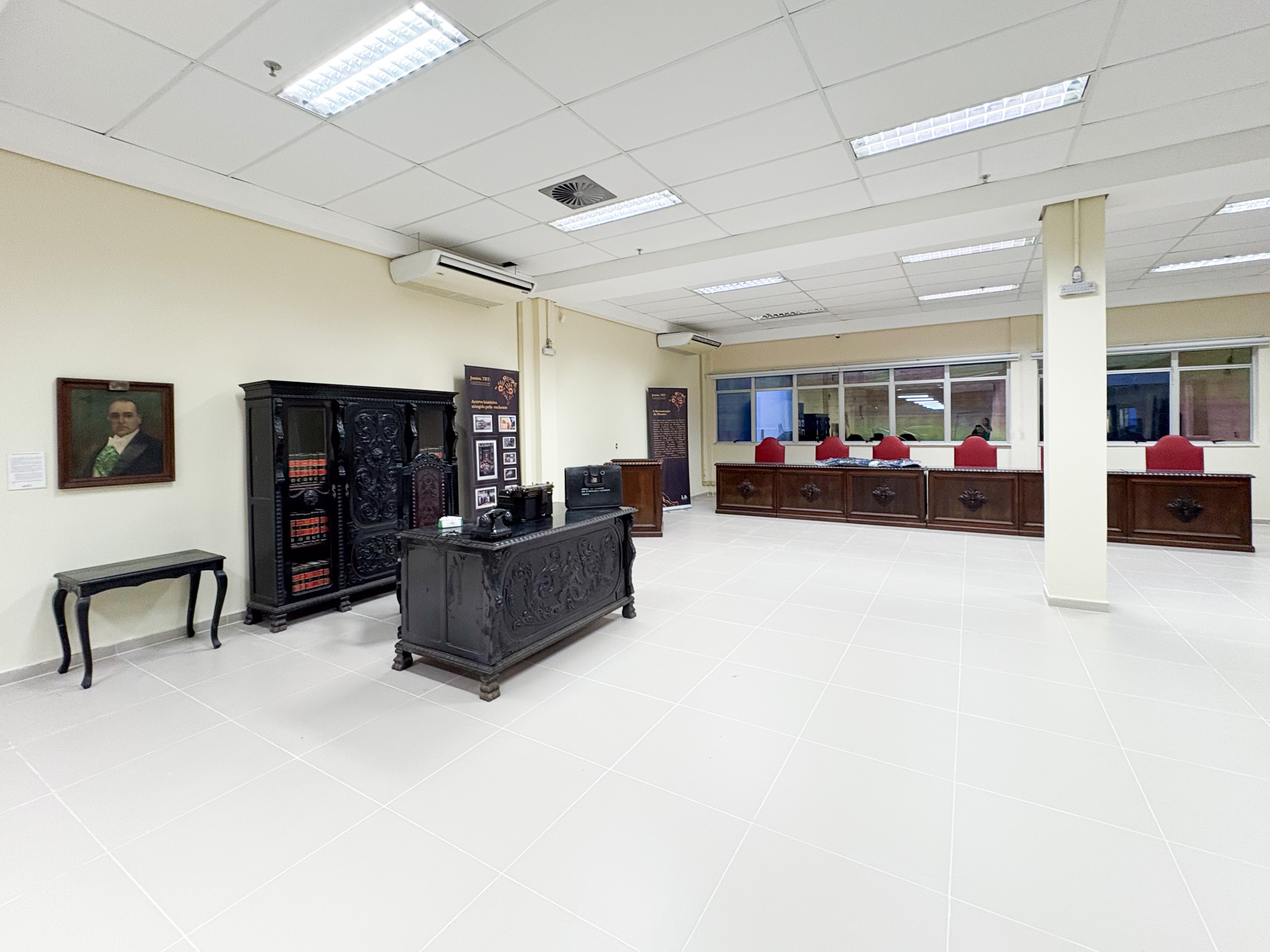 Foto geral da sala, com bancadas de madeira na esquerda, o barco ao fundo, a porta de vidro no fundo à esquerda, uma mesa ao centro, uma porta no centro ao fundo e um sofá na direta.