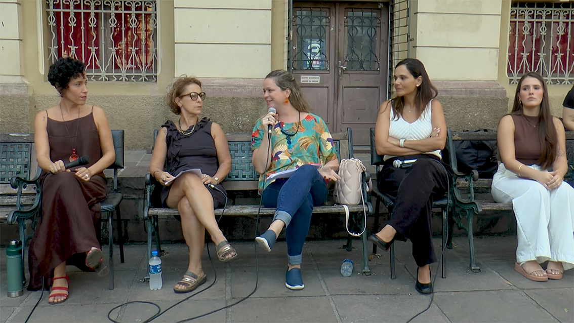 Em frente ao prédio da Faculdade de Direito da UFRGS, cinco mulheres conversam, sentadas em bancos de praça. Da direita para esquerda, estão: a professora Valdete Souto Severo, a professora municipal de Porto Alegre Isabel Medeiros, a socióloga Aline Kerber, a professora de Direito Vanessa Gonçalves e a acadêmica Camila Rodrigues