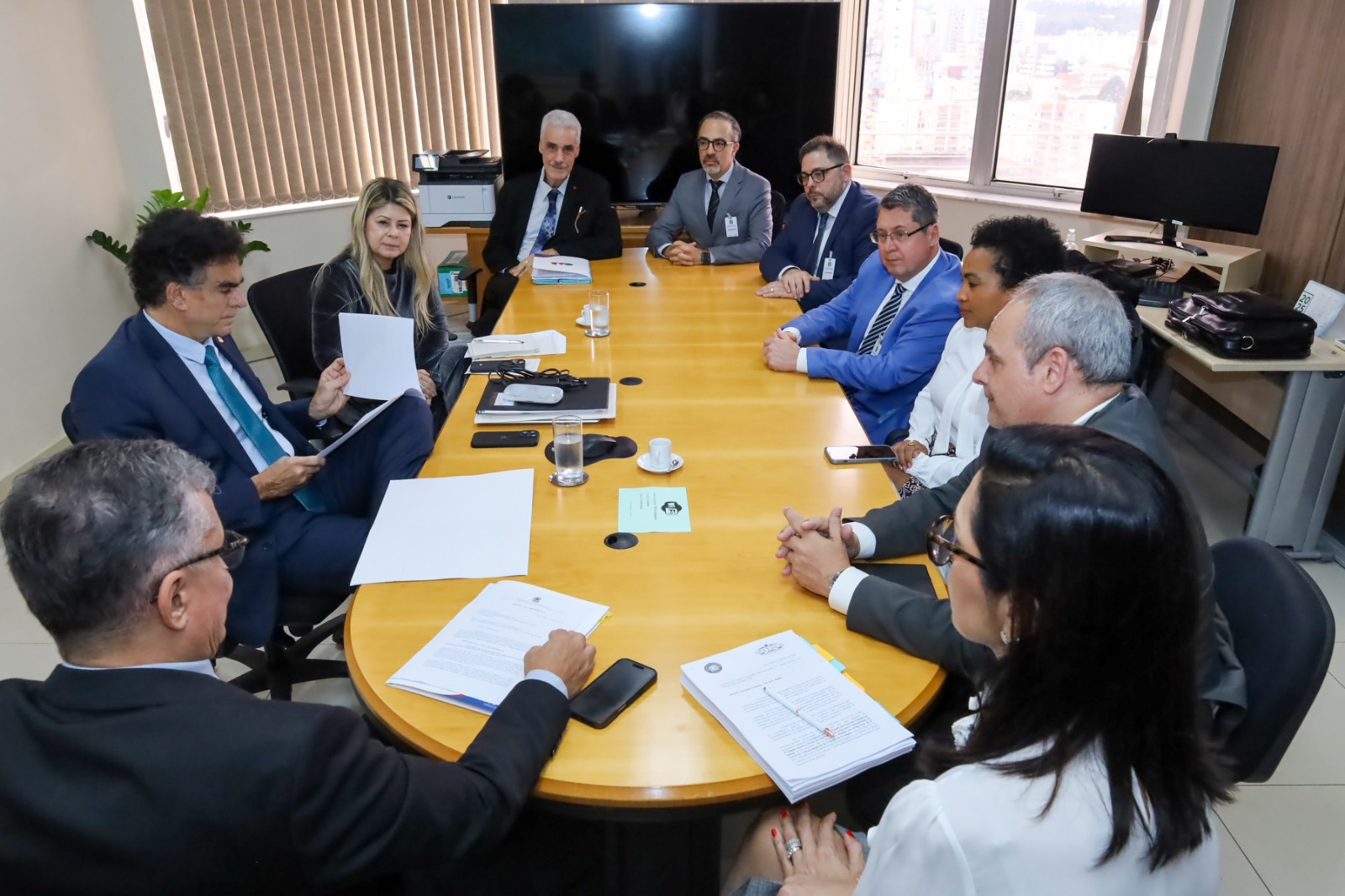 Foto de diversas pessoas reunidas em volta de uma mesa, com o corregedor-geral lendo papeis.