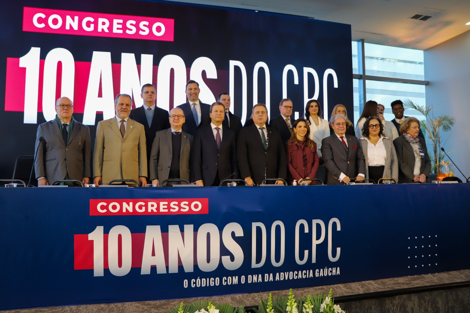 A foto mostra uma série de autoridades posando para foto em cima de um palco, com telão de fundo.
