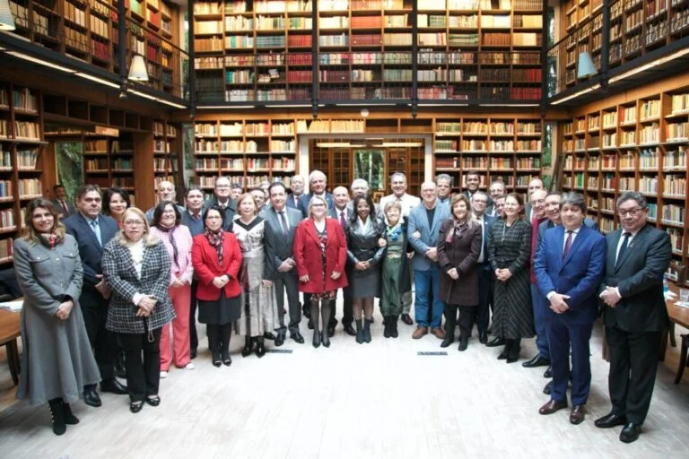 Grupo de cerca de 30 pessoas posando para foto em uma biblioteca com estantes altas cheias de livros, em ambiente iluminado e formal.