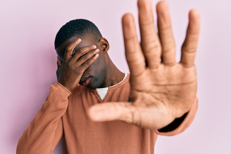 Foto ilustrativa de um homem negro com uma mão tapando os olhos e a outra estendida em sinal de "pare".