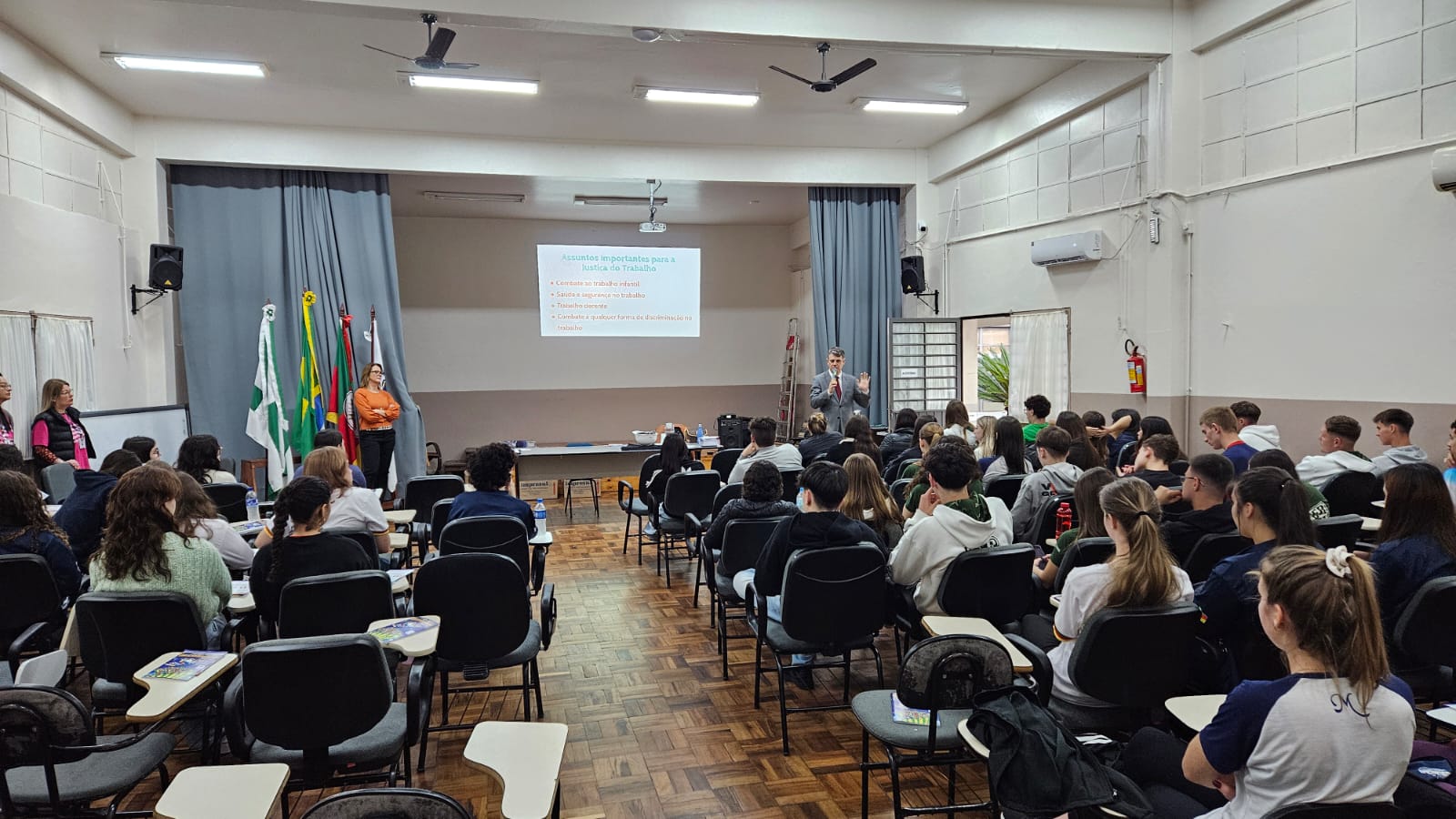 Vista ampla do auditório do Colégio Estadual Professor Mantovani com dezenas de estudantes assistindo à apresentação