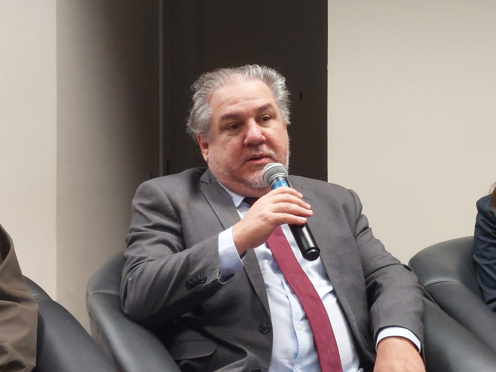 O desembargador Marcos Fagundes Salomão fala ao microfone, sentado numa cadeira preta. Atrás dele, um painel com um telão exibe "MPT Ministério Público do Trabalho no Rio Grande do Sul".