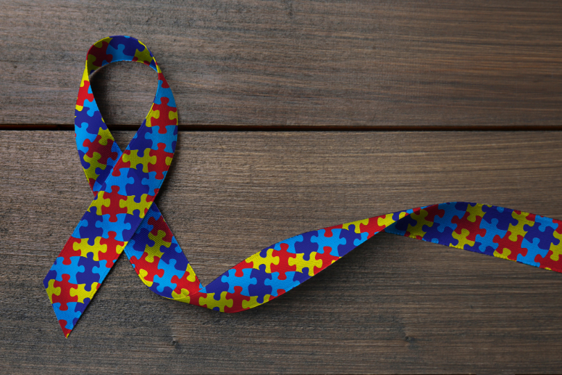 Laço colorido representando a conscientização sobre o autismo, sobre fundo de madeira.