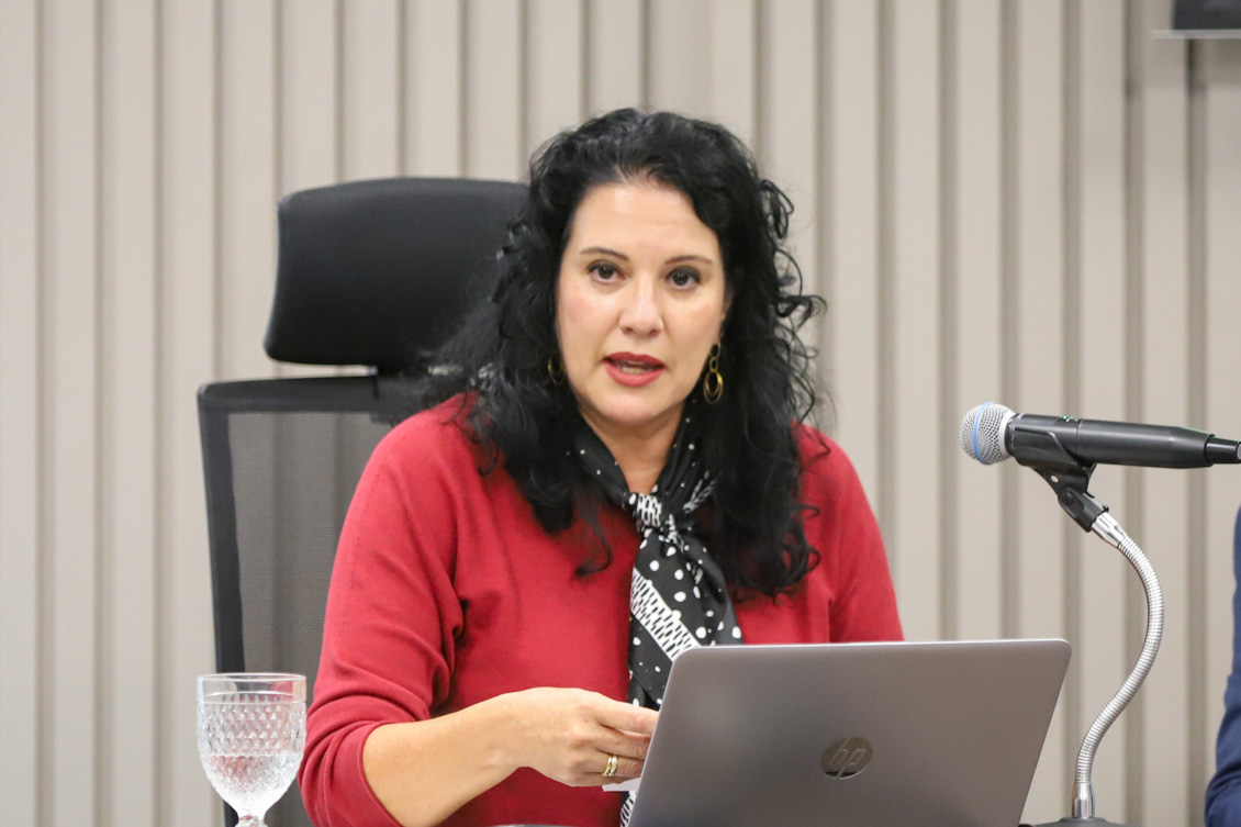a assessora Iara está sentada à mesa, falando ao microfone.