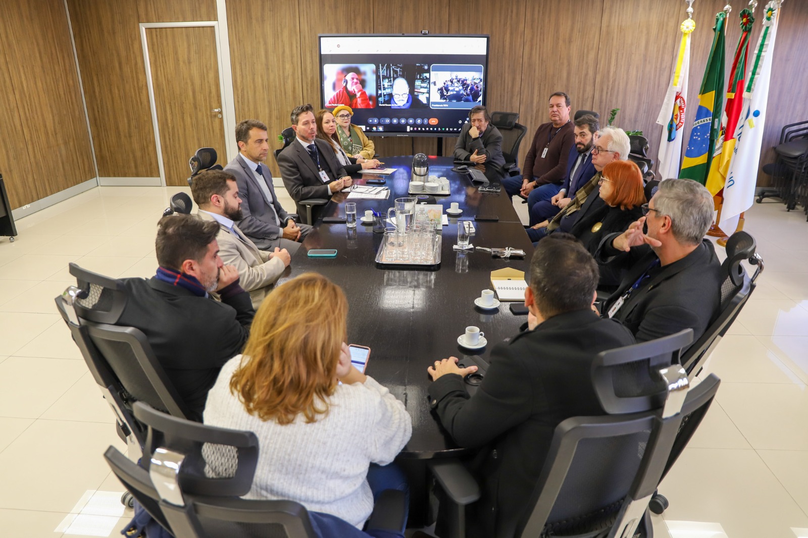 A foto mostra integrantes do Gabinete de Crise Climática do TRT-RS reunidos em volta de uma mesa, com alguns participando on-line num telão.