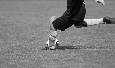 Detalhe da cintura para baixo em preto e branco de atleta de posse da bola no campo de futebol