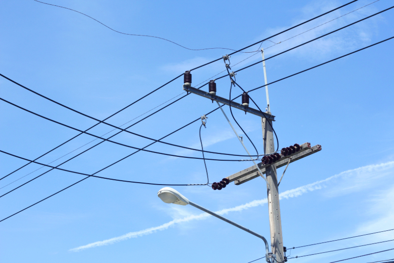 Poste elétrico e fiação. Ao fundo, céu azul.