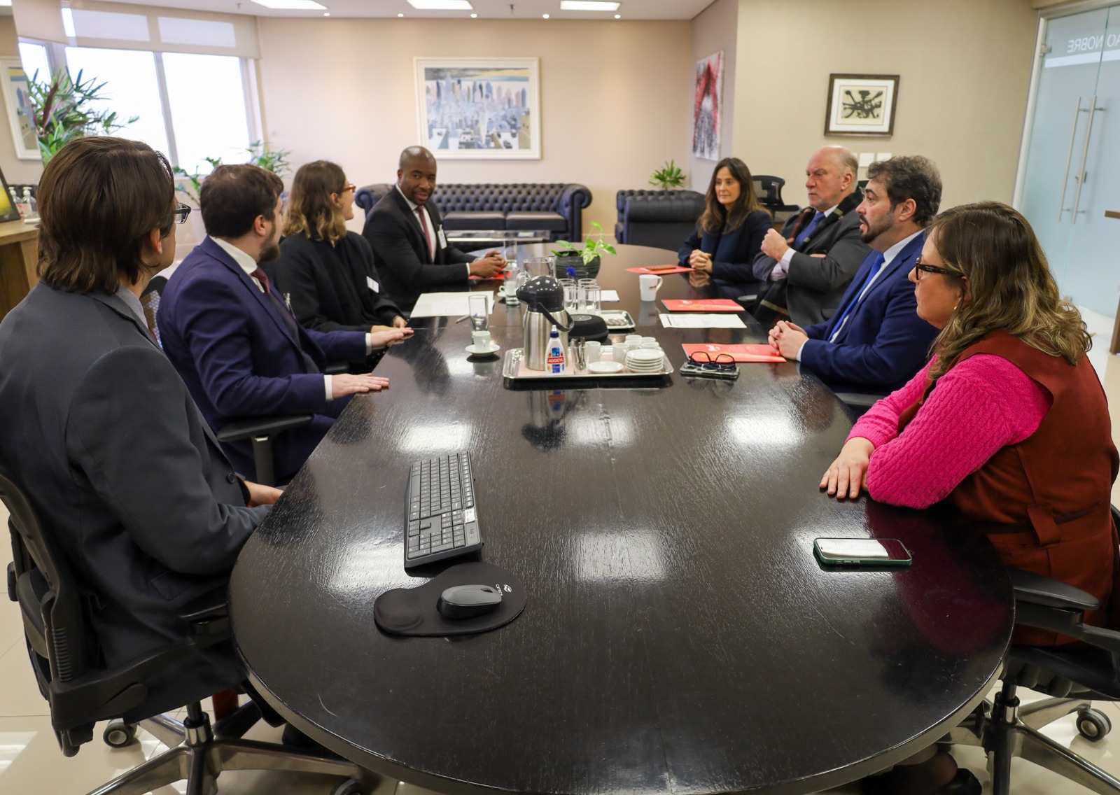 A foto mostra os presentes na reunião sentados em volta de uma mesa.