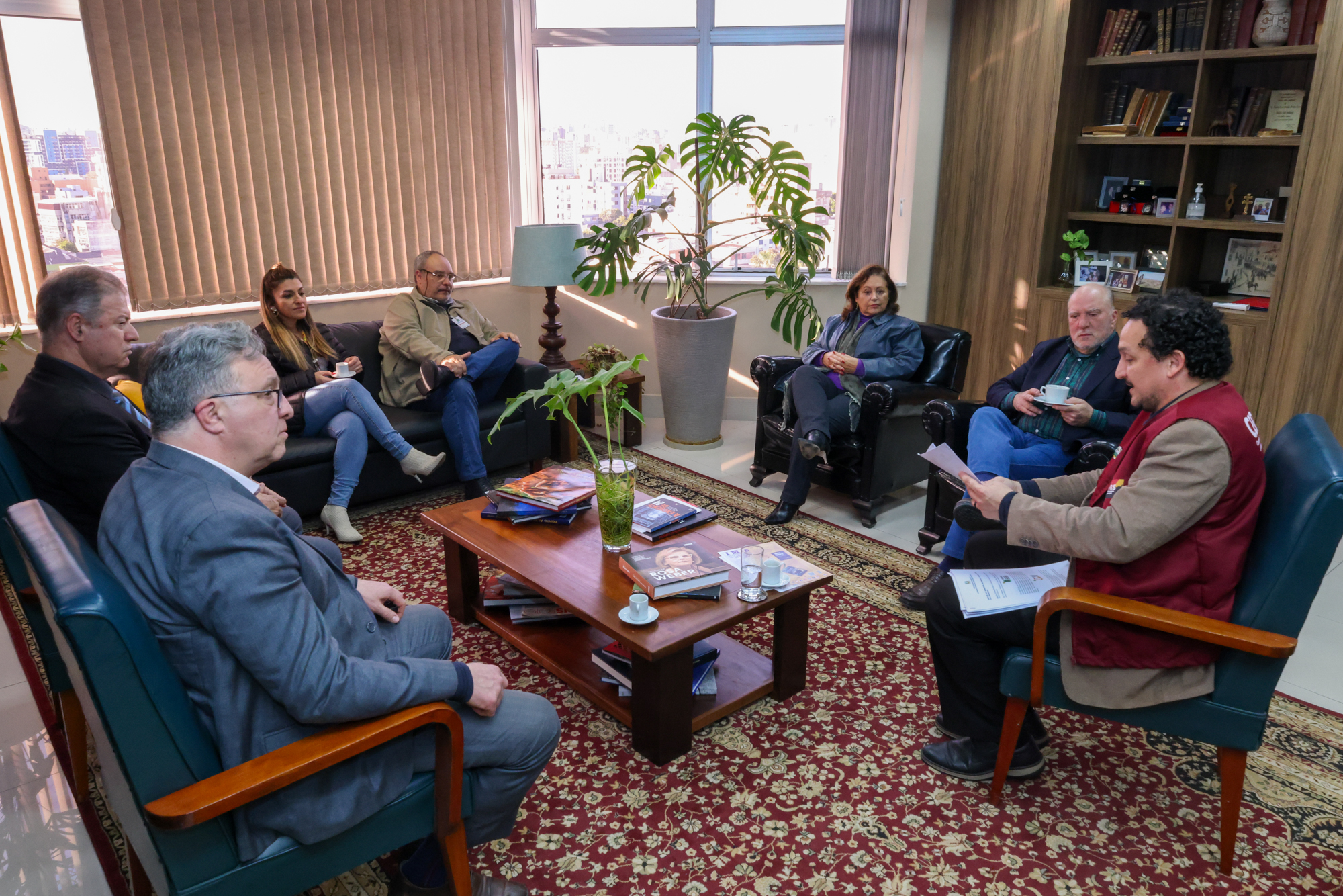 Foto da reunião, em ângulo aberto, mostrando os participantes sentados