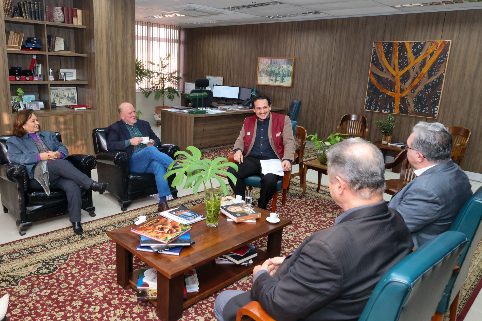 Foto da reunião, em ângulo aberto, mostrando os participantes sentados