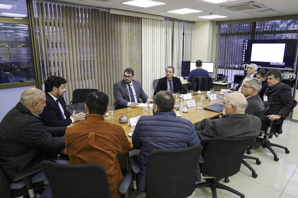 12 pessoas aparecem em uma mesa de negociações, com alguém digitando de costas ao fundo. O vice-presidente aparece no centro da imagem.