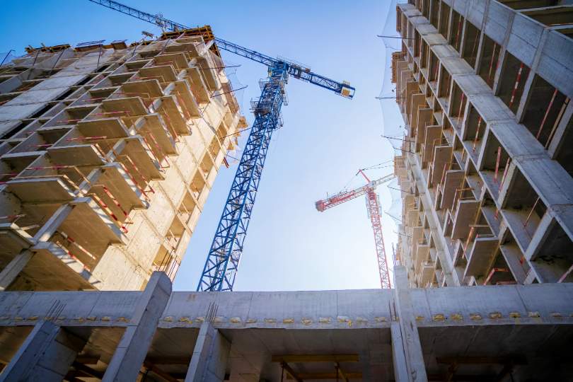 Dois prédios em obras e duas gruas entre eles, imagem de baixo para cima.