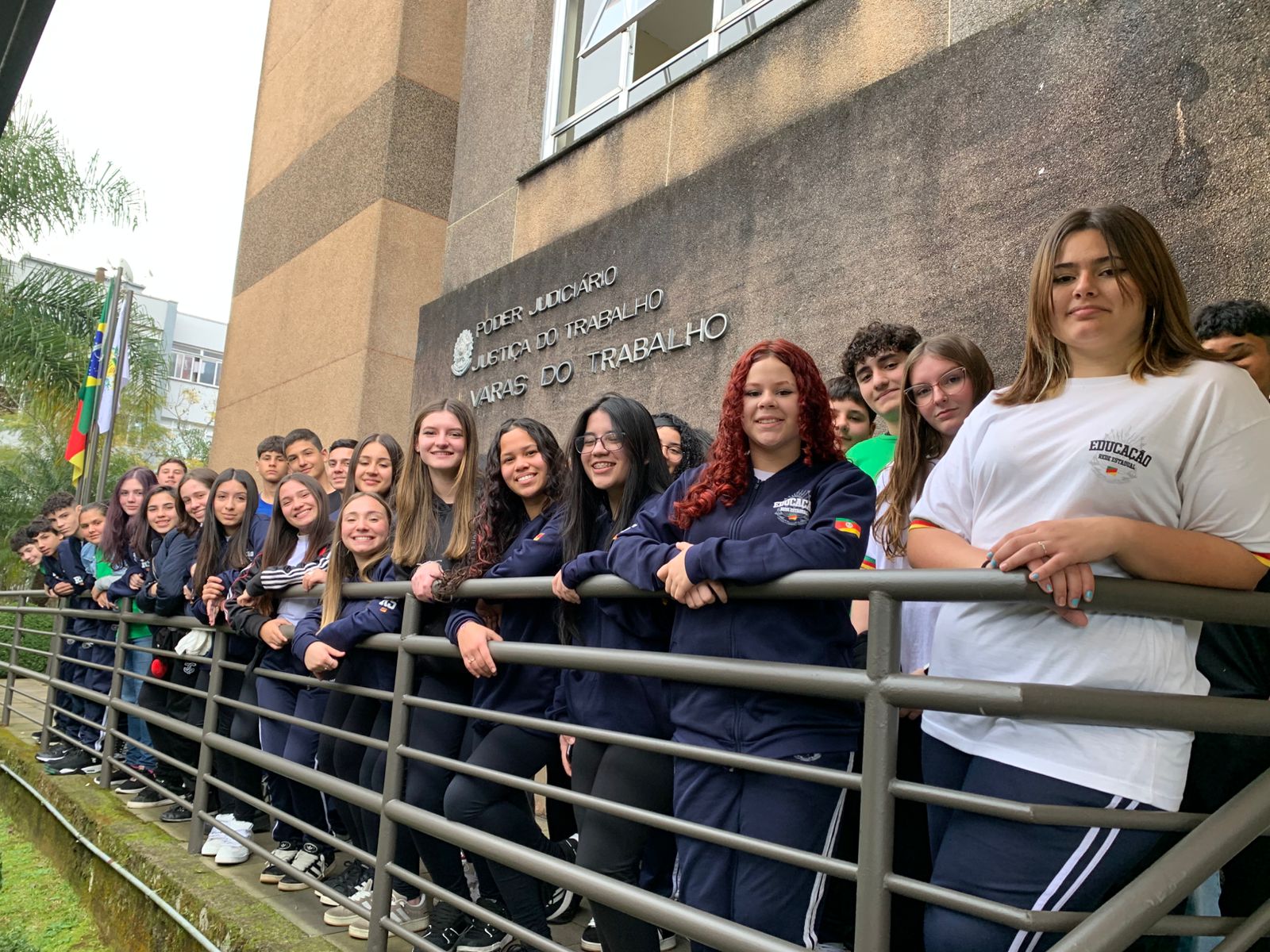 Um grande grupo de adolescentes posa sorridente em frente ao prédio do Foro Trabalhista. Eles estão uniformizados e acompanhados por professores.