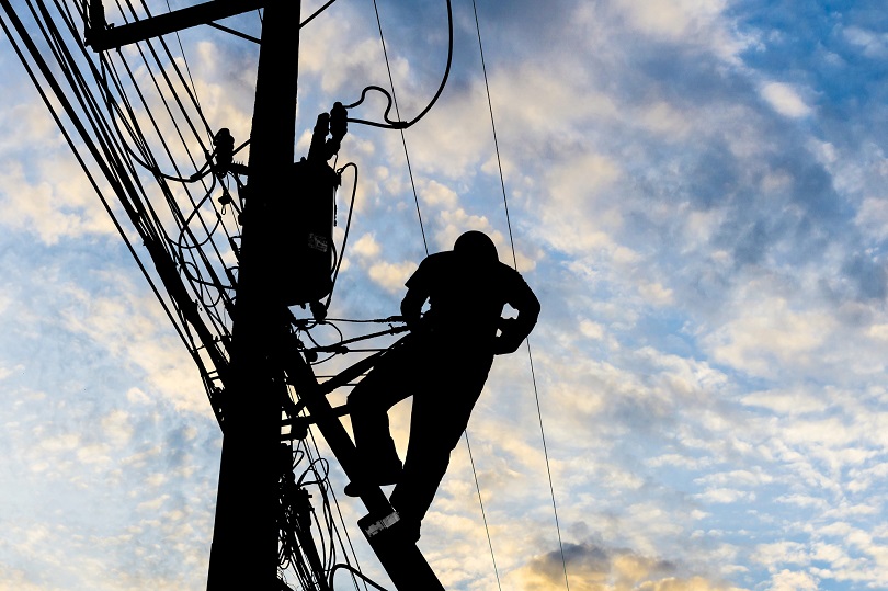 Foto ilustrativa de uma pessoa trabalhando no topo de um poste de energia elétrica.