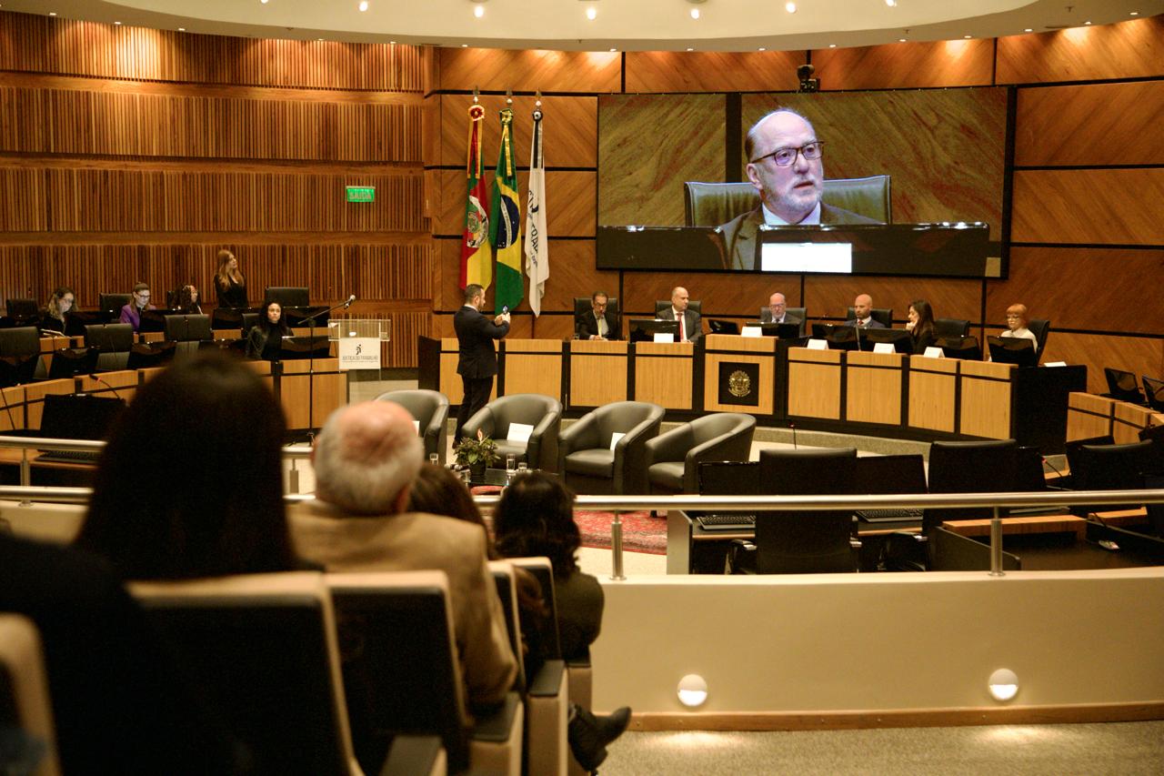 A foto mostra o presidente Martins Costa discursando e sua imagem sendo reproduzida no telão.