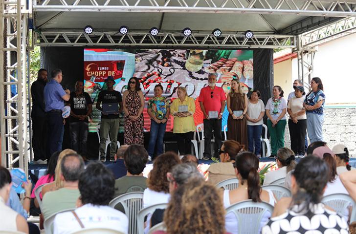 Foto mostra um momento da visita, em que magistrados estão em um palco, conversando com representantes locais da comunidade. Na foto também aparece o público sentado.