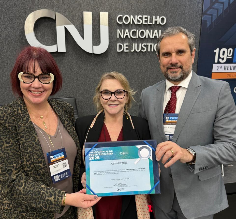 Três pessoas aparecem sorrindo para a foto, segurando um certificado. Ao fundo, na parede, aparece o logo do CNJ. 