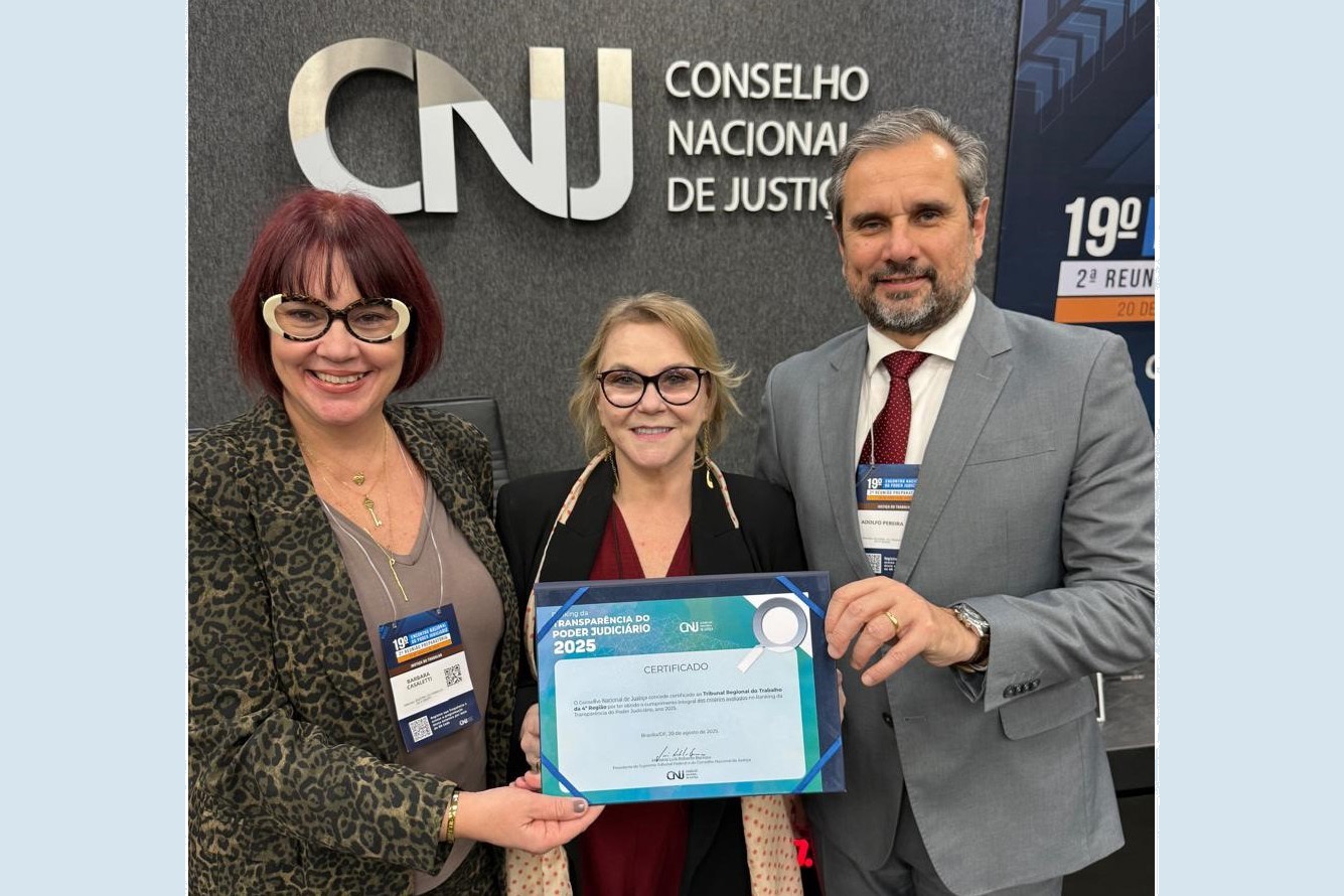 Três pessoas aparecem sorrindo para a foto, segurando um certificado. Ao fundo, na parede, aparece o logo do CNJ.