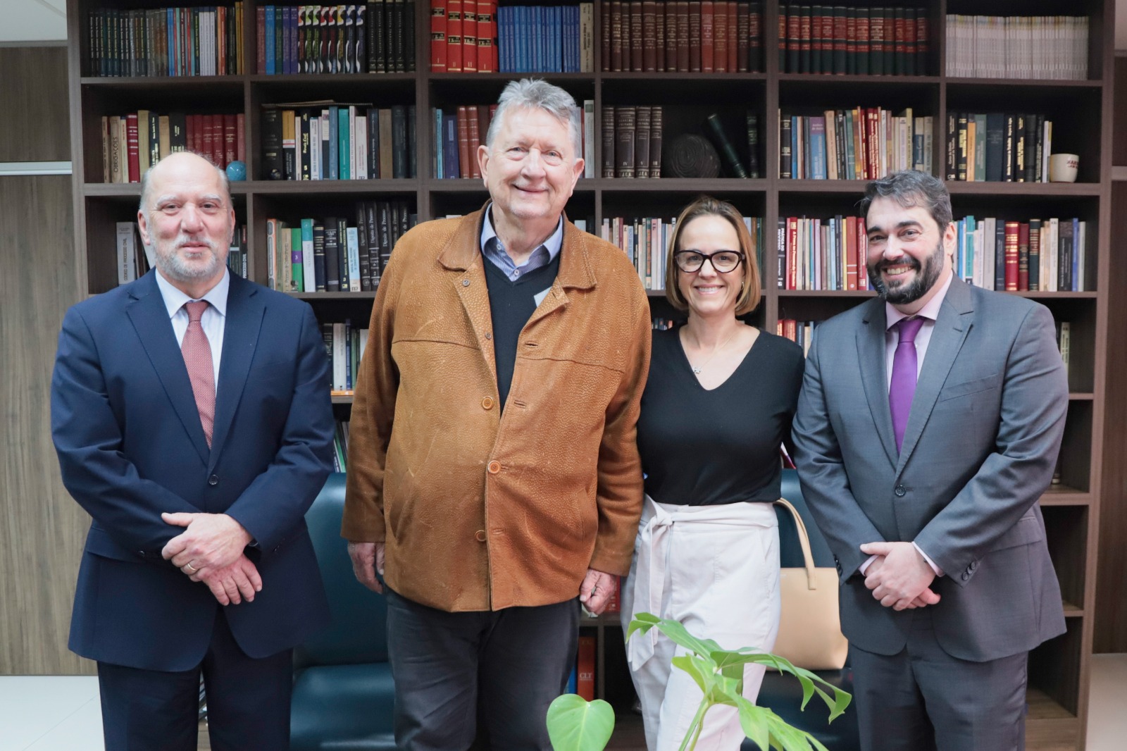 Os quatro posam sorrindo, de pé, em frente à estante com livros.