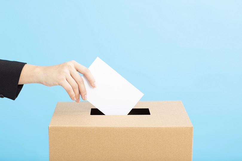 Foto ilustrativa da mão de uma mulher que coloca uma cédula em urna de votação.