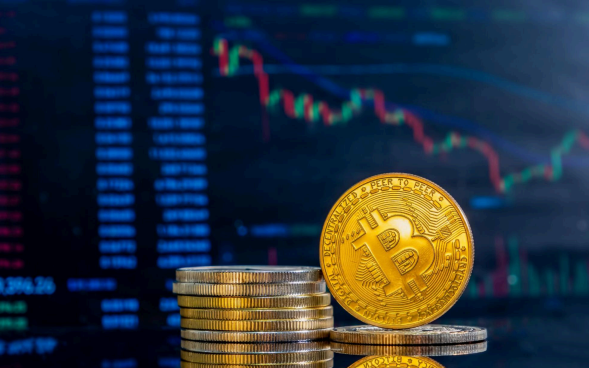 várias moedas douradas empilhadas, em destaque uma moeda com o símbolo do Bitcoin na frente. Ao fundo, aparece uma tela desfocada com gráficos de linhas e números