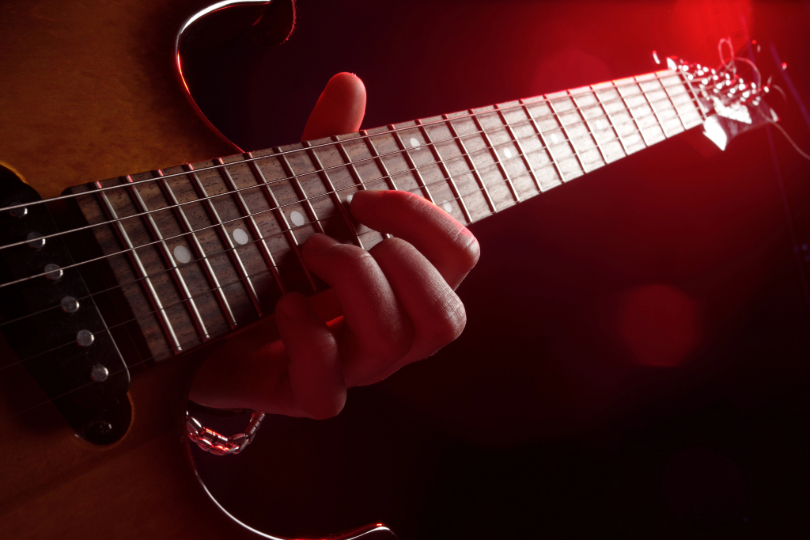 homem toca guitarra. Não há imagem do rosto. Instrumento tem tons de vermelho preto.