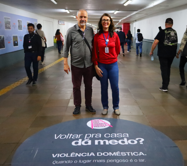 servidores posam para foto no corredor subterrâneo da estação, ao lado de um adesivo no chão com os dizeres “Voltar pra casa dá medo? Violência doméstica. Quando o lugar mais perigoso é o lar”.