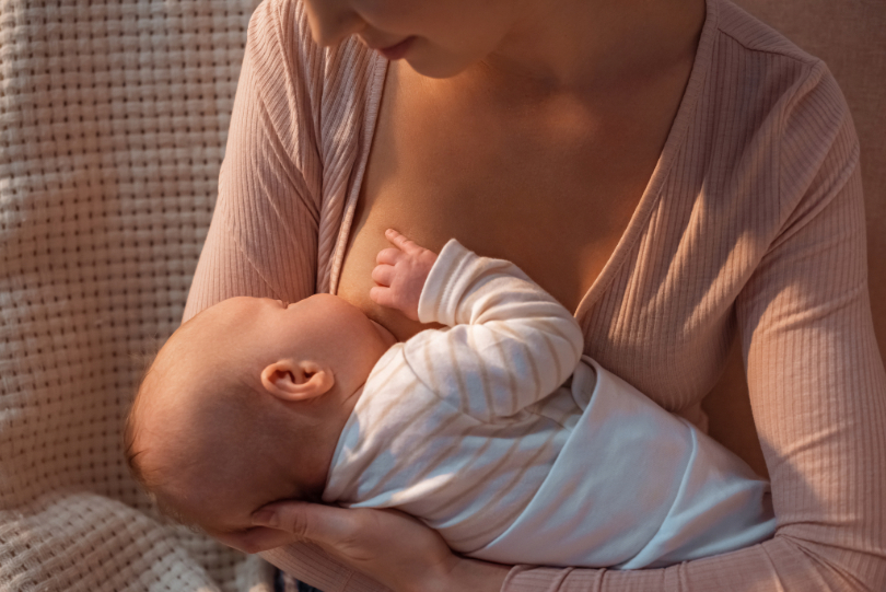 mãe amamenta bebê. Ambos têm a pele clara. Ela usa blusa bege. Não há imagem do rosto.