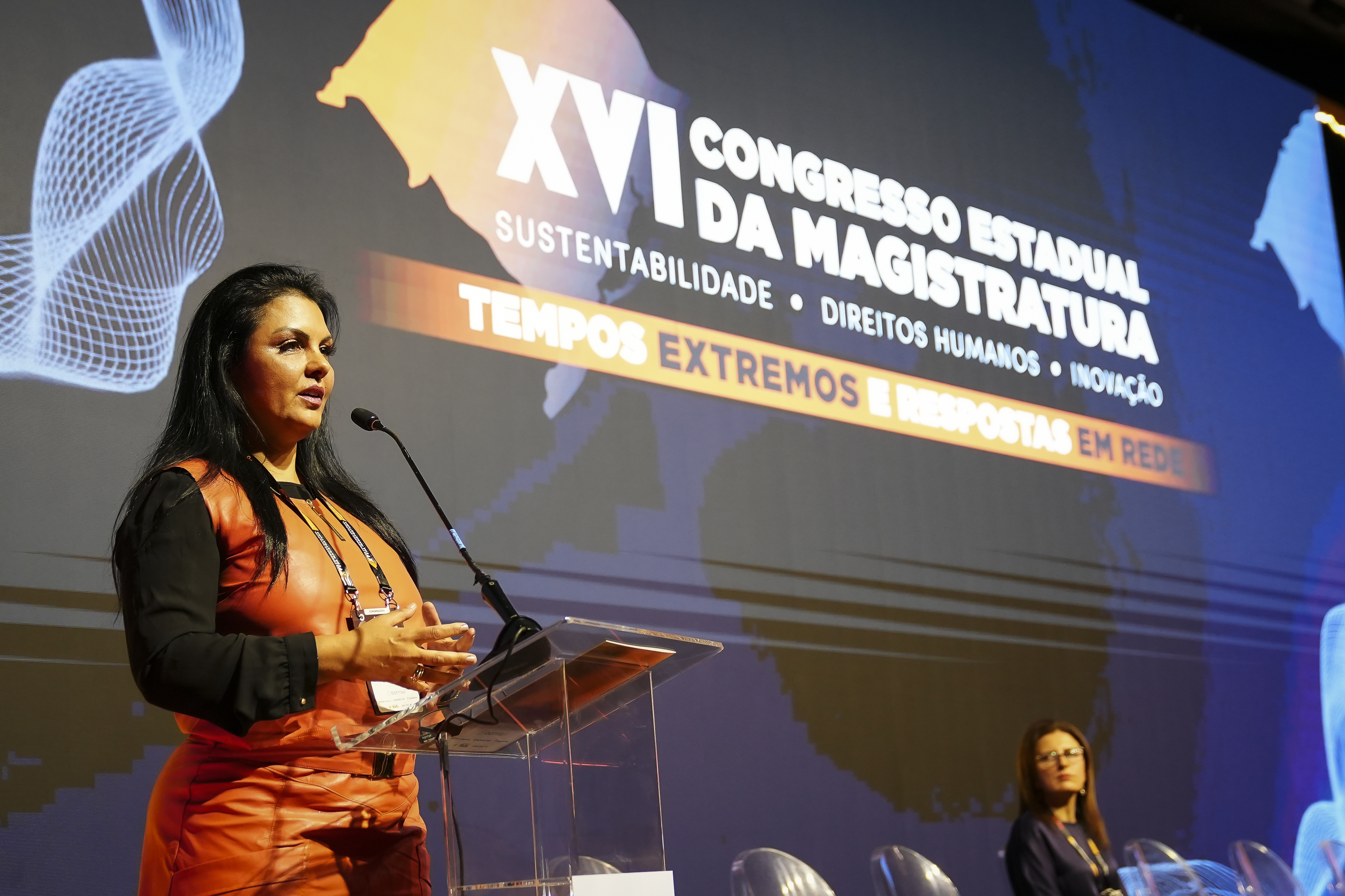 A desembargadora Tânia palestrando no púlpito. Ela veste laranja com preto, ao fundo está a logo do XIV Congresso da AJURIS.