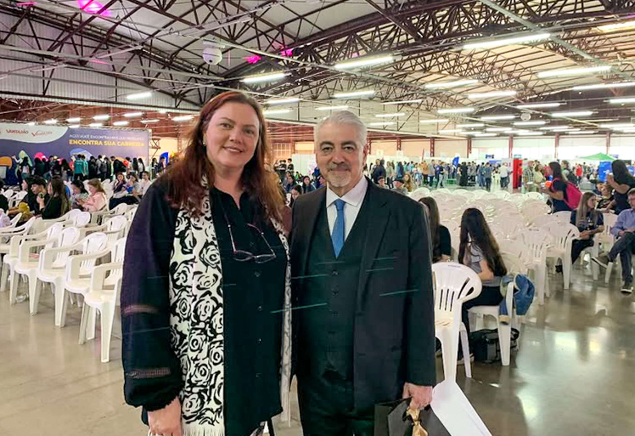 Denise Bampi e Marcelo Porto. Ao fundo, jovens sentados em cadeiras brancas de plástico.