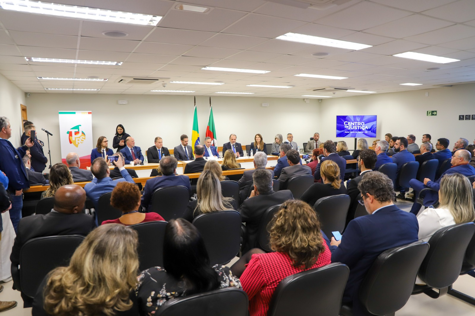 Foto em angulo aberto da cerimonia, mostrando público e mesa oficial