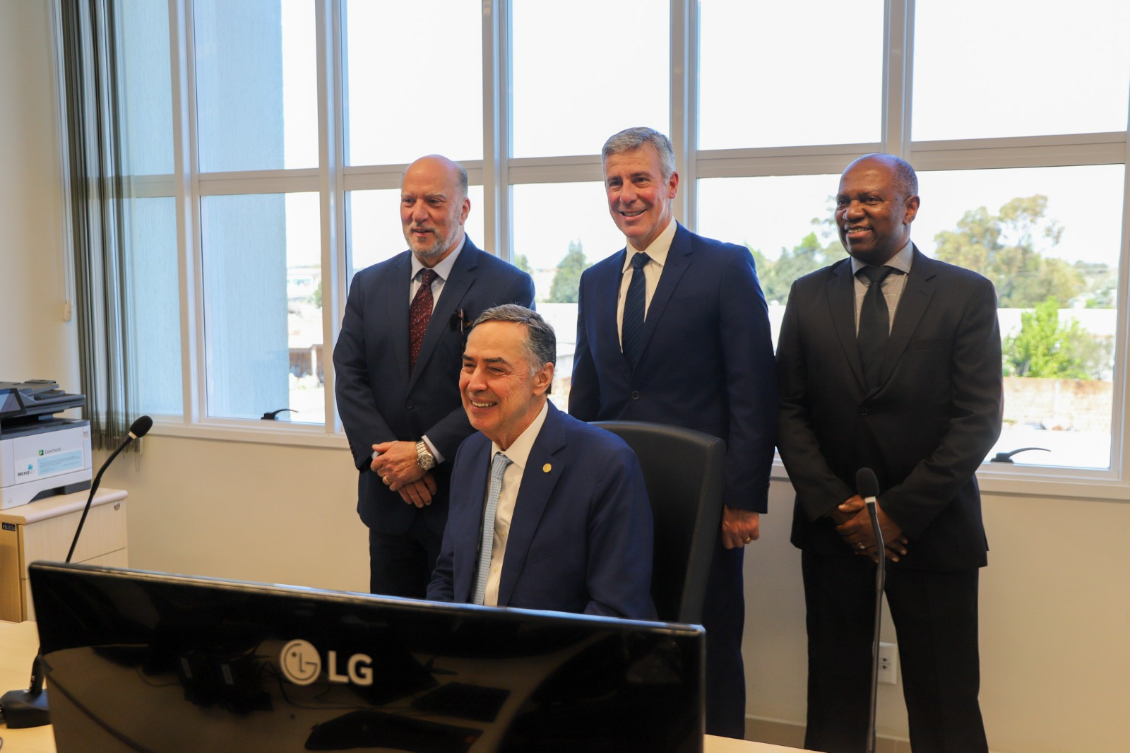 Ministro Barroso, na sala de audiências da VT de Santa Vitória do Palmar, sentado na cadeira do juiz. Atrás dele, o juiz André Vieira, o desembargador Martins Costa e o diretor da VT, Jesus Samuel da Rocha