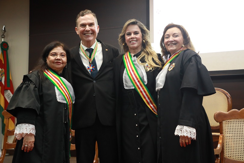 Desembargador Clóvis posa para a foto com a medalha ao lado de 3 mulheres na cerimônia.