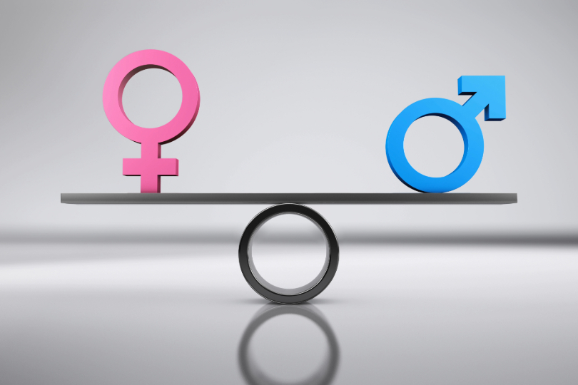 Igualdade de gênero: gangorra cinza sustenta os símbolos de masculino e feminino, nas cores azul e rosa, respectivamente.