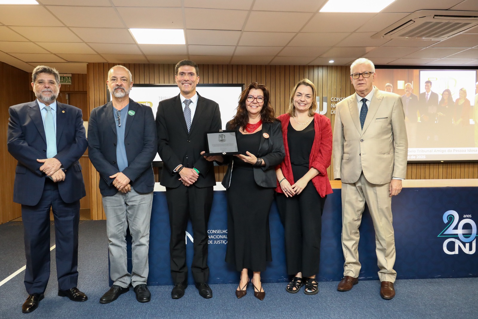 Juíza Lúcia Matos, Gabriela Lenz de Lacerda, Márcio Meireles Martins e outros três ministros, lado a lado, na sede do CNJ. A juíza Lúcia está com a placa alusiva ao reconhecimento nas mãos.