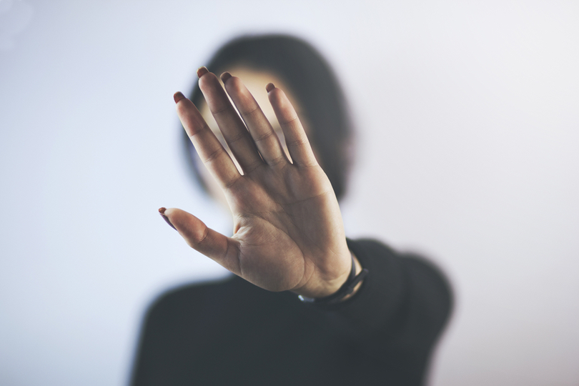 Foto de uma mulher com a mão espalmada para a câmera, em sinal de "pare". A mão está em primeiro plano, cobrindo seu rosto.