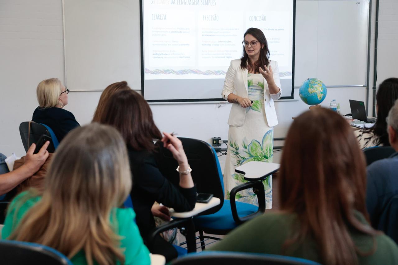 Alunos em primeiro plano e Lara ao fundo de pé e falando.